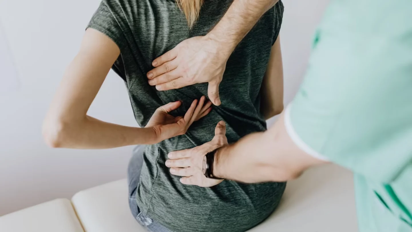 From above of crop faceless slim female patient sitting on examination couch and indicating osteopath in uniform pain spot