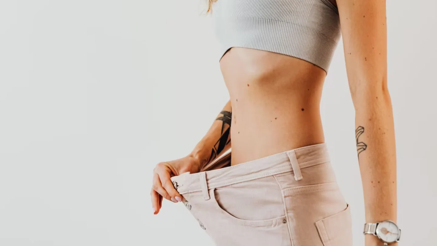 Close-up of a woman in oversized jeans symbolizing weight loss in a studio setting.