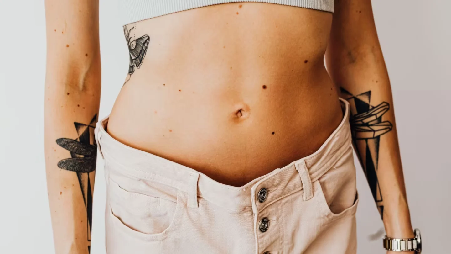 Close-up of a tattooed woman's torso wearing high-waisted pants, showcasing body art and style.