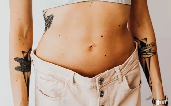 A woman displaying weight loss by wearing oversized pants and crop top, showing tattoos.