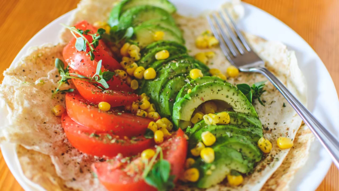 Vibrant salad with avocado, tomato, and corn on flatbread, topped with herbs, perfect for a healthy meal.