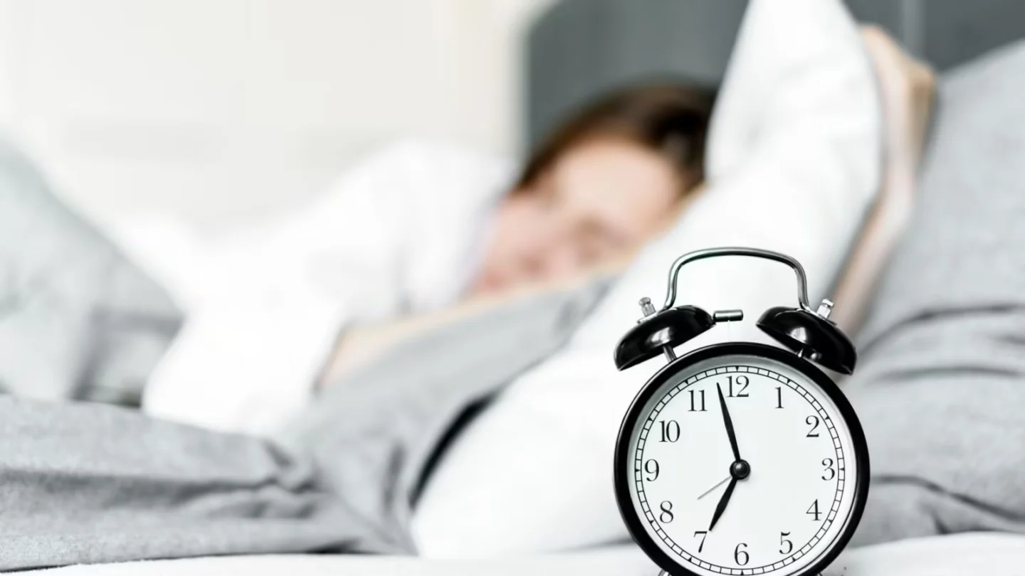 Retro alarm clock sits by a sleeping woman in a cozy bedroom setting.