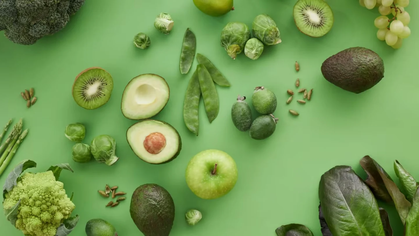 Variety of fresh green fruits and vegetables on a matching background, showcasing healthy organic produce.