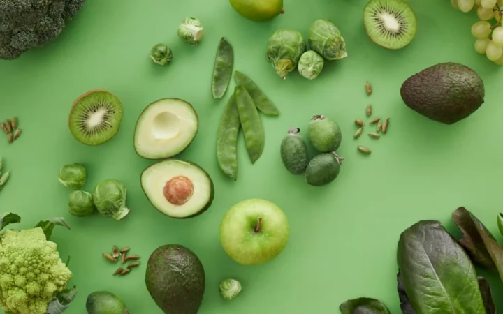A variety of fresh green fruits and vegetables on a matching background, showcasing healthy organic produce.