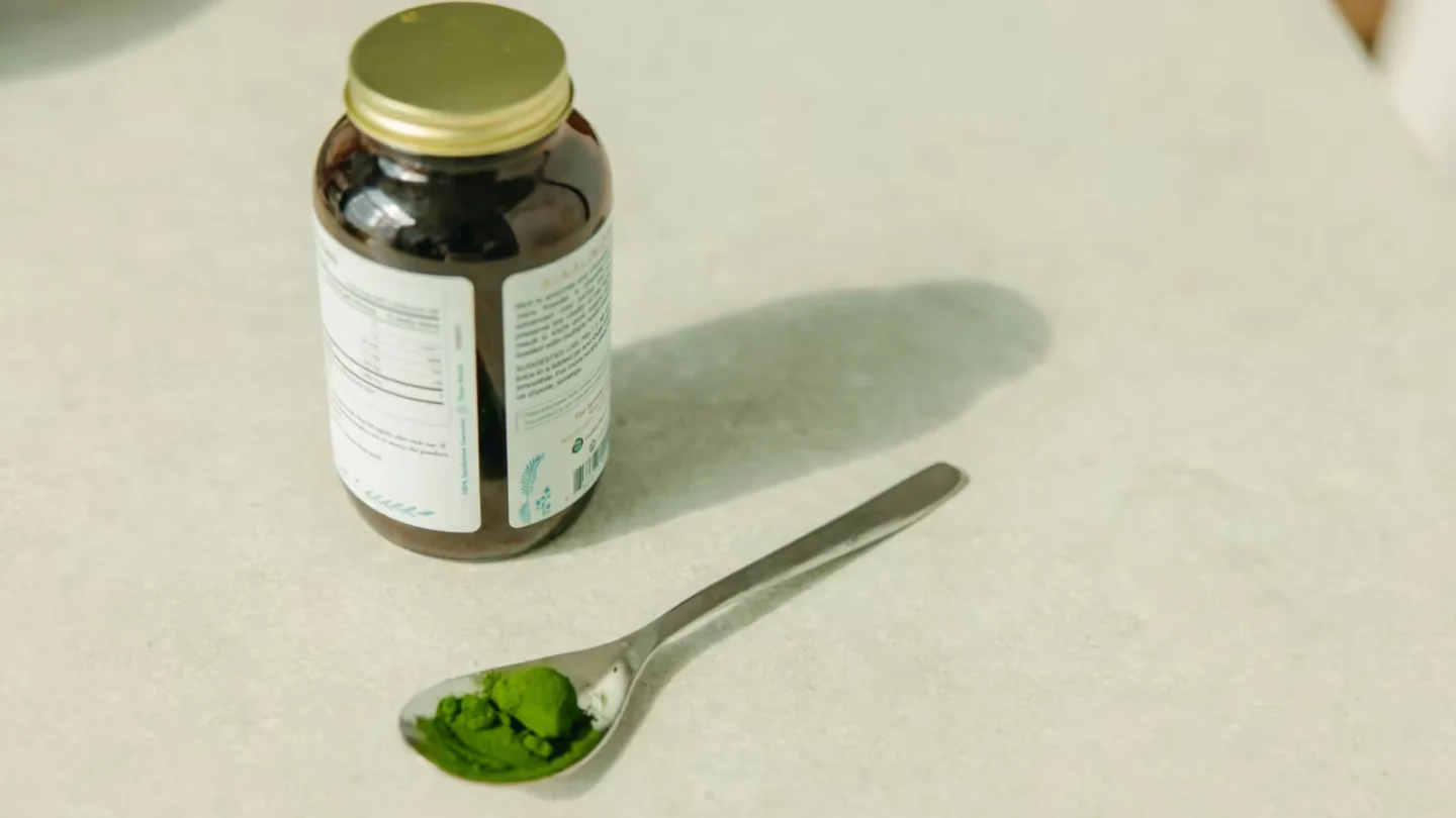 Close-up of a jar and a spoon with green powder, ideal for healthcare and wellness themes.