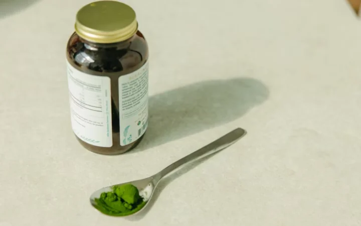 Close-up of a jar and a spoon with green powder, ideal for healthcare and wellness themes.
