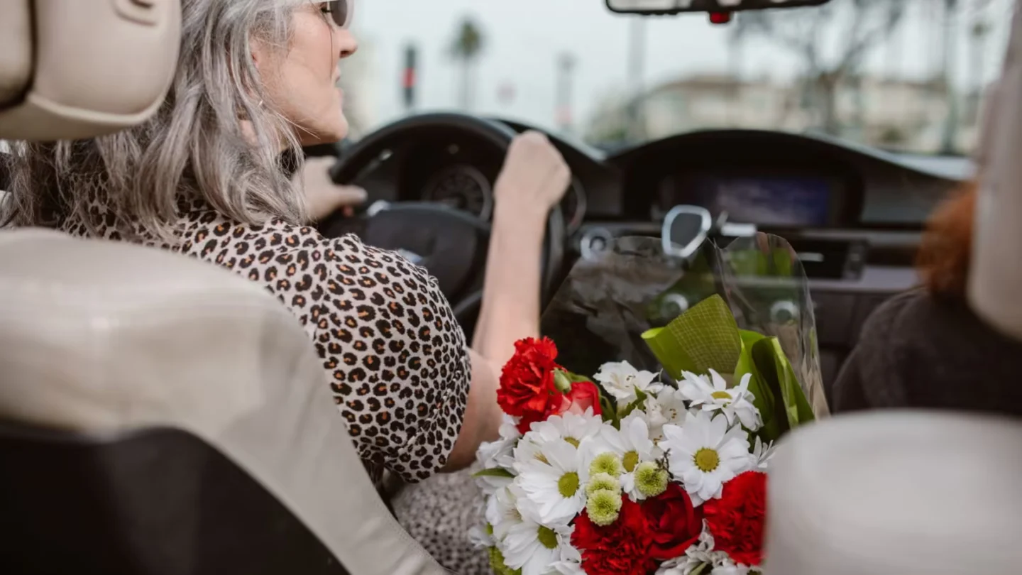 Woman driving, holding a bouquet of colorful flowers in a car.