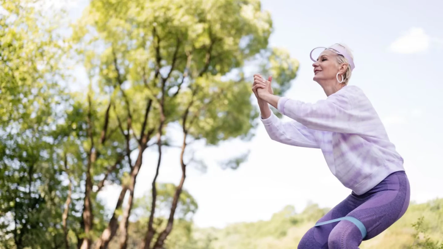 Senior woman exercises in a park with a resistance band, embracing a healthy lifestyle.