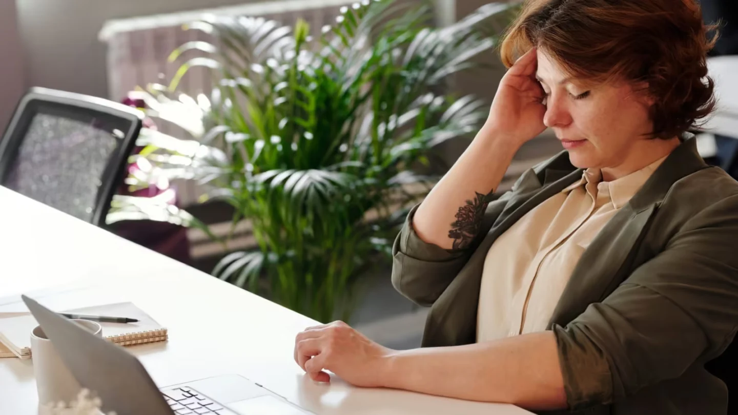 Businesswoman feeling stressed at her home office desk while working on her laptop.