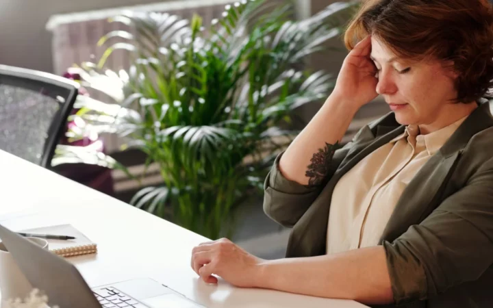 Businesswoman feeling stressed at her home office desk while working on her laptop.