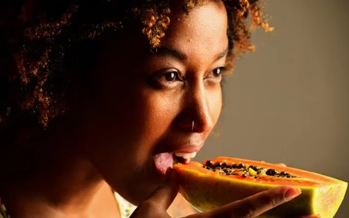 A woman eating a slice of fresh papaya