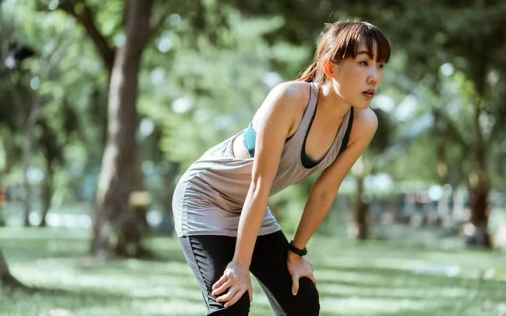 A woman resting her hands on her knees after running outdoors