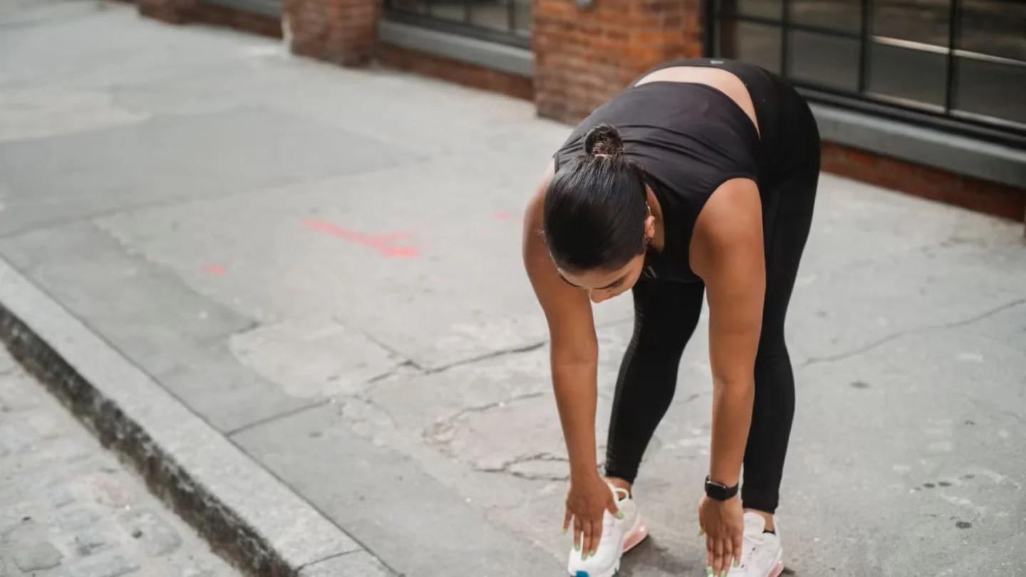 Woman in athletic wear performs stretching exercises on a city sidewalk, promoting a healthy lifestyle.