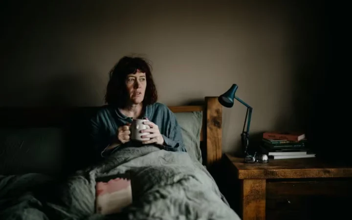 A woman sitting awake in bed at night holding a mug