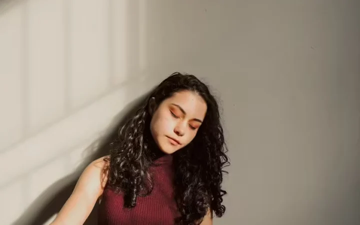 A woman resting against a wall with her eyes closed