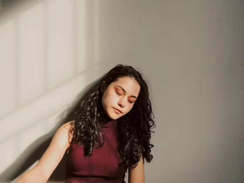 A woman resting against a wall with her eyes closed