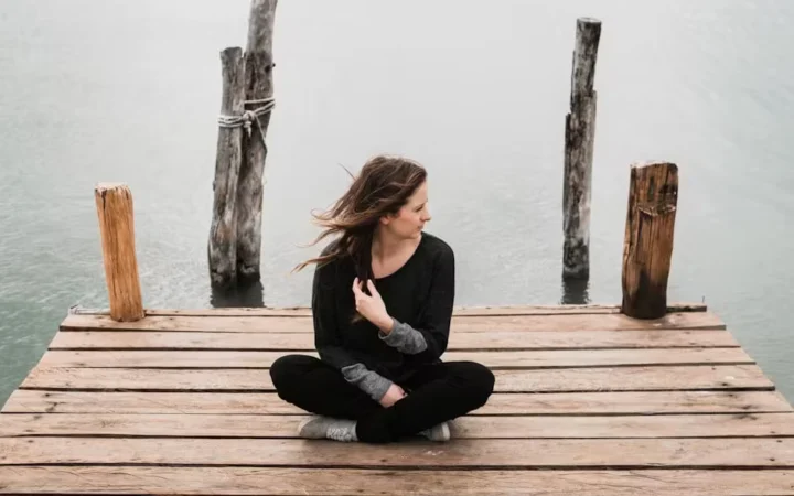 A woman sitting cross-legged at the end of a wooden jetty