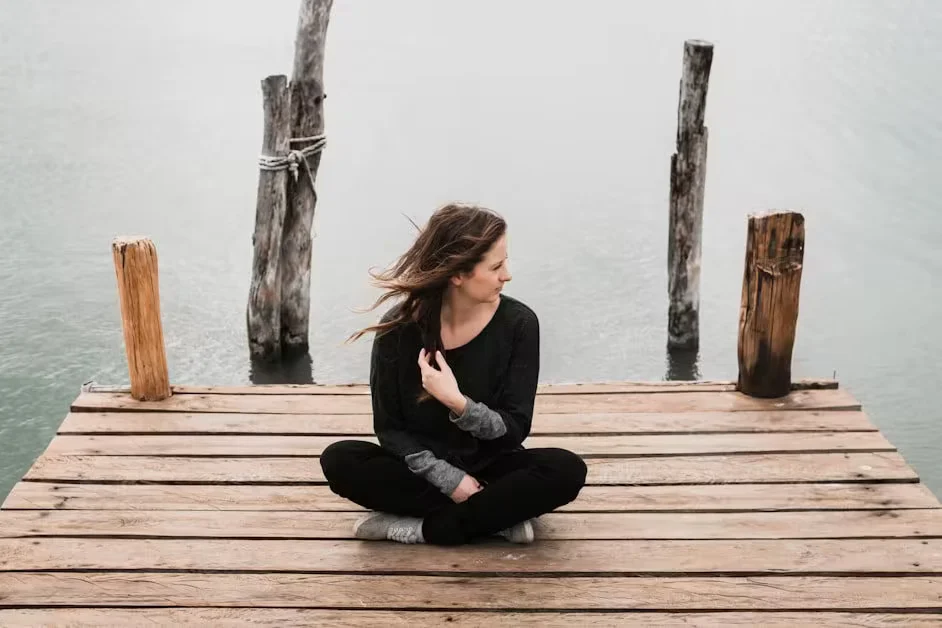 A woman sitting cross-legged at the end of a wooden jetty