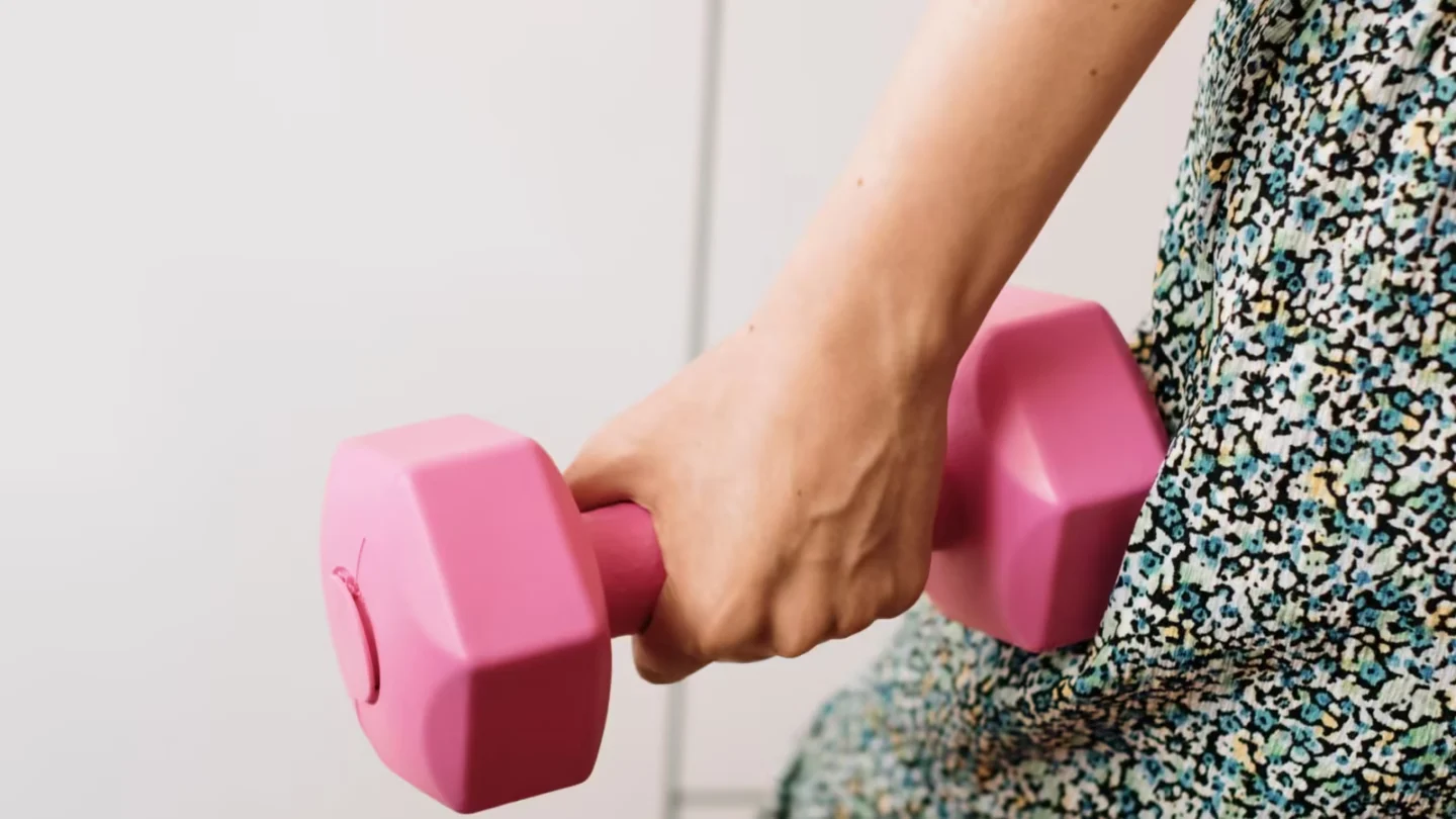 Close-up of a woman's hand holding a pink dumbbell, symbolizing fitness and strength.