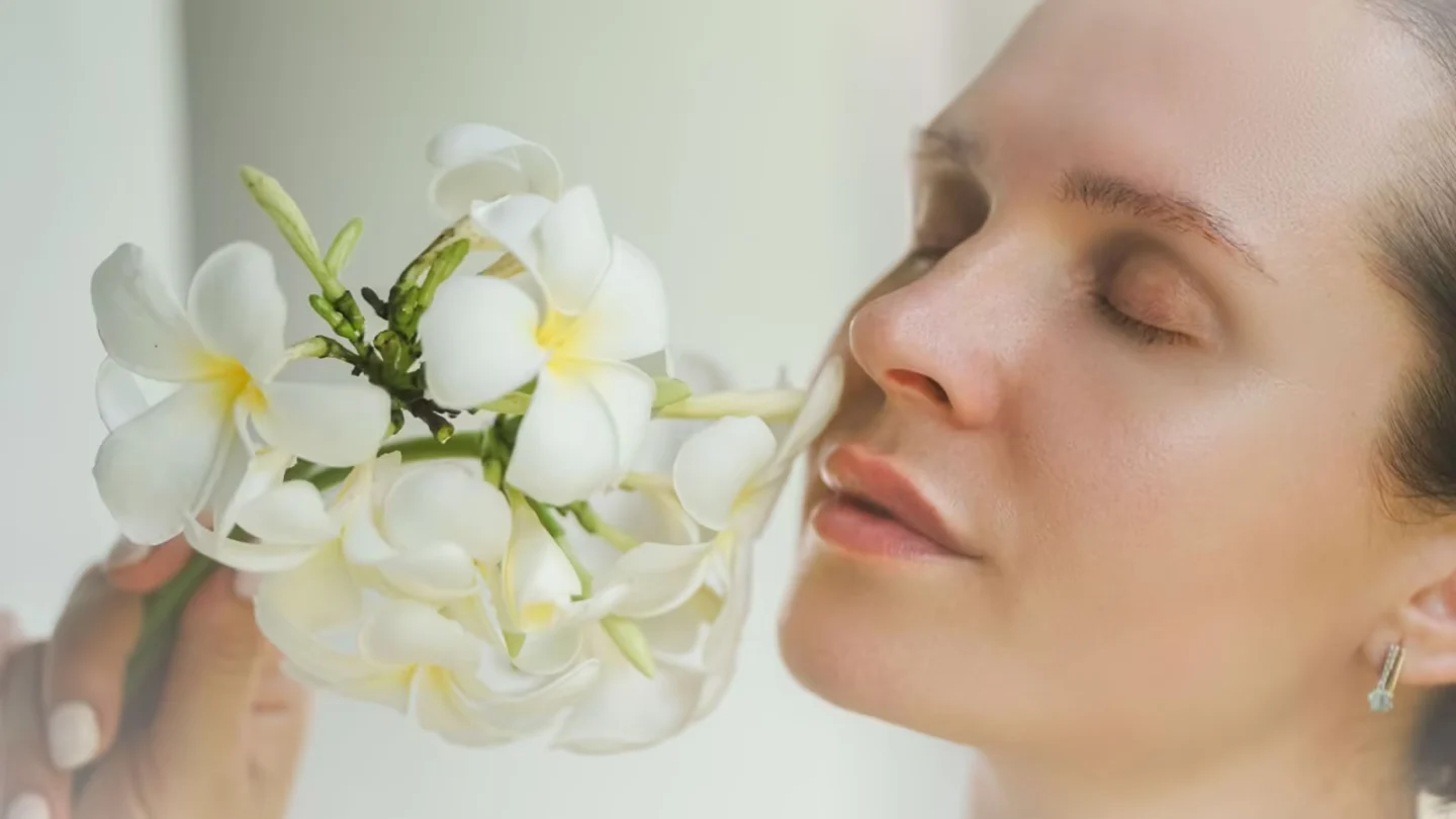 Close-up portrait of a woman holding white frangipani flowers with eyes closed, depicting serenity and natural beauty.