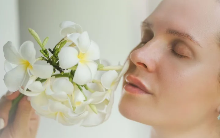 Close-up portrait of a woman holding white frangipani flowers with eyes closed, depicting serenity and natural beauty.