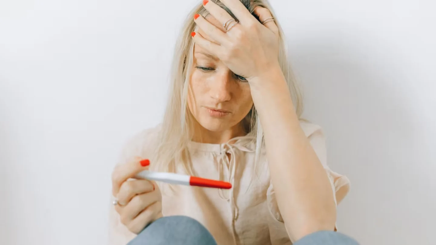 Concerned woman looks at a pregnancy test, reflecting emotions of anxiety and uncertainty.