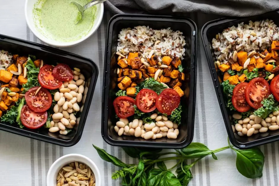 Meal prep containers of rice, roasted vegetables, beans and tomatoes