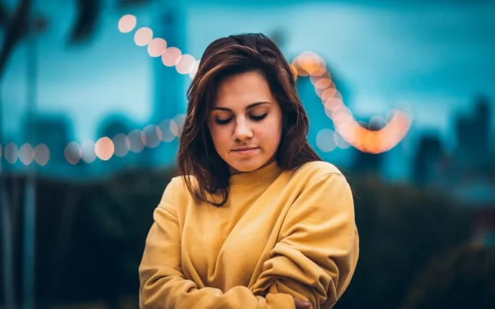 A woman in a yellow jumper with her arms folded, looking down
