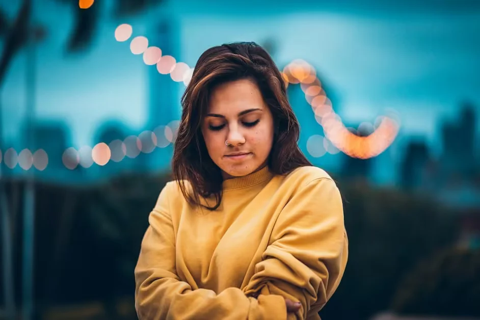 A woman in a yellow jumper with her arms folded, looking down
