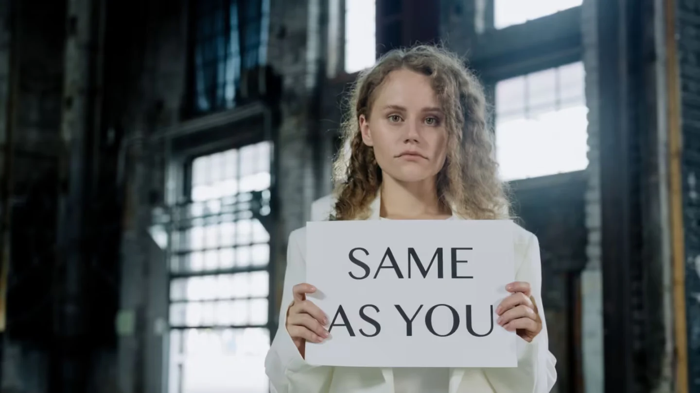 Caucasian woman in white outfit holding sign with text in urban setting.