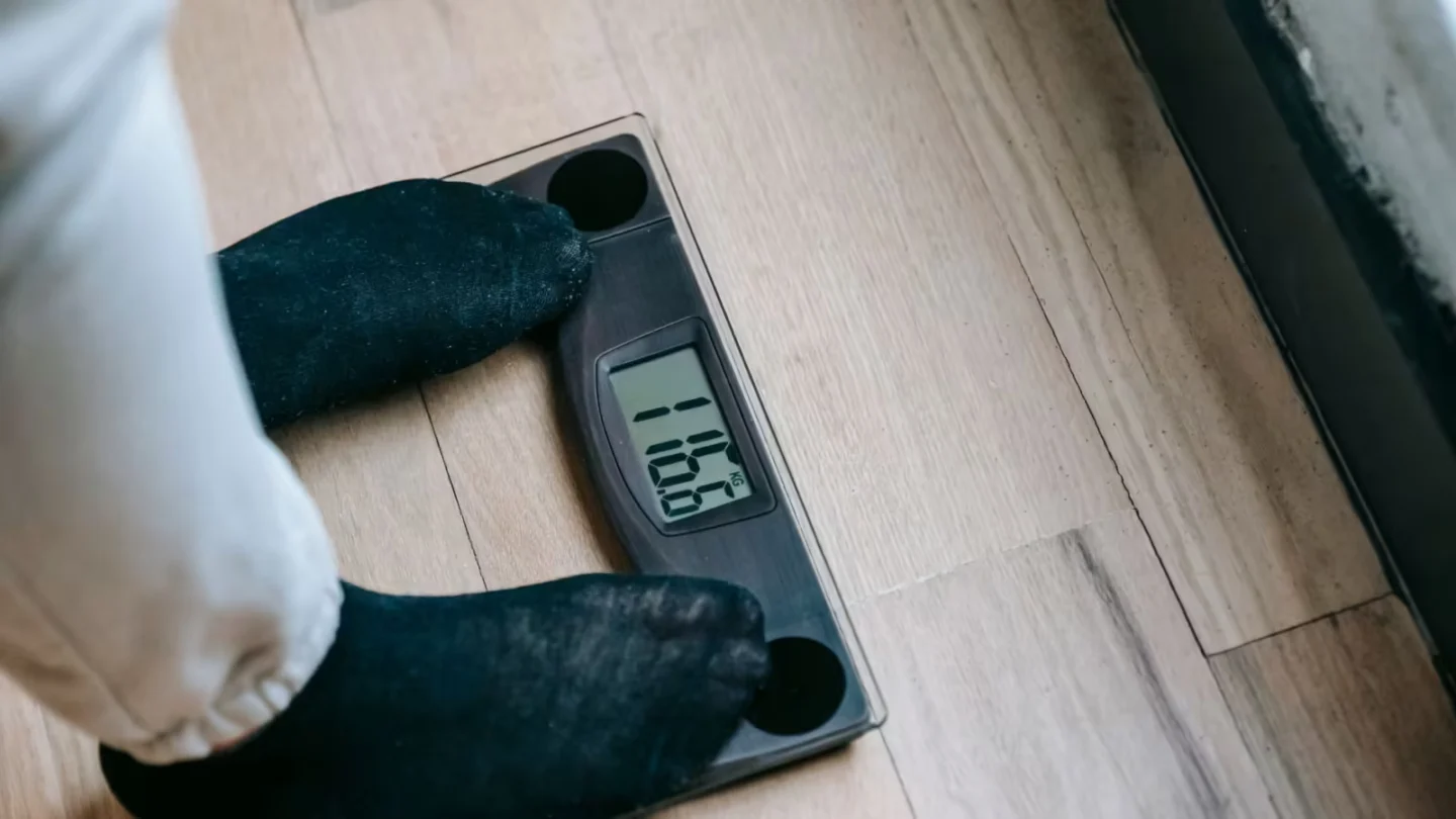 From above of unrecognizable person in socks standing on electronic weighing scales while checking weight on parquet during
