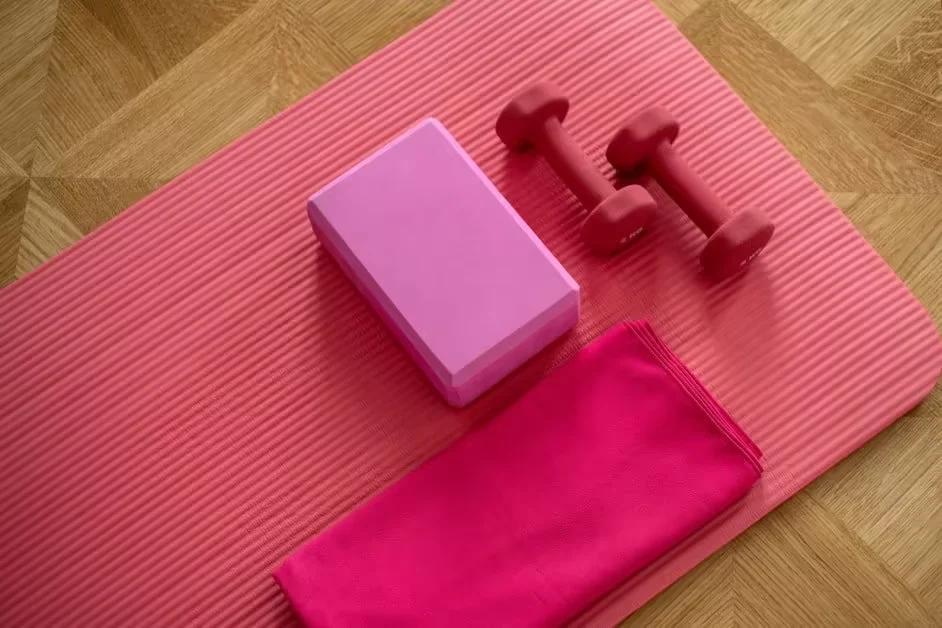 A pink yoga mat with blocks and light dumbbells