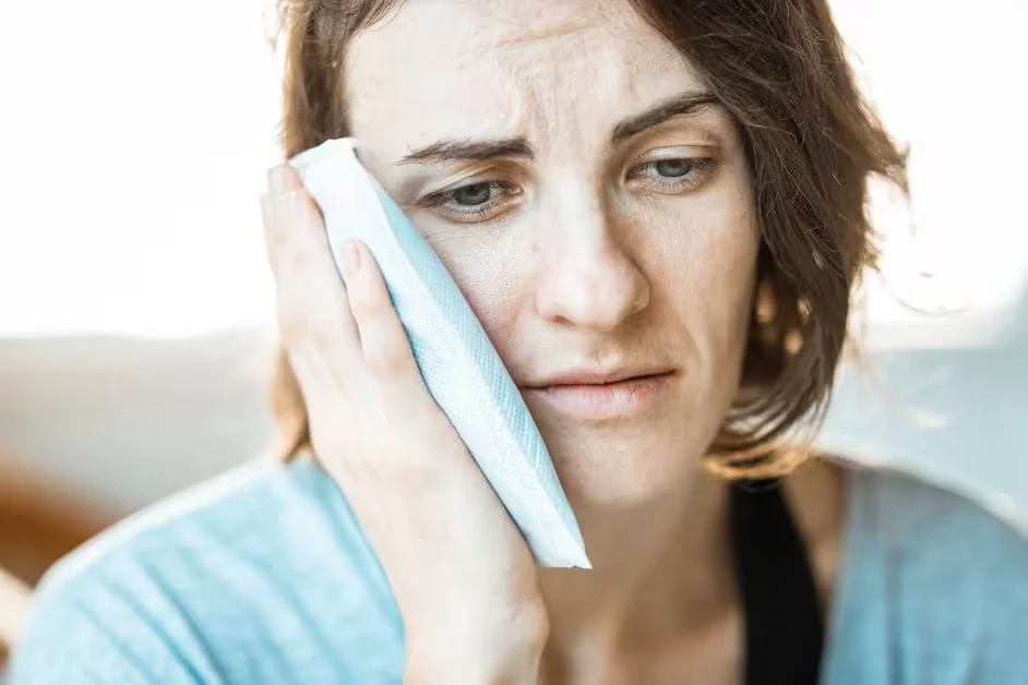 A woman holding a cold pack against her cheek