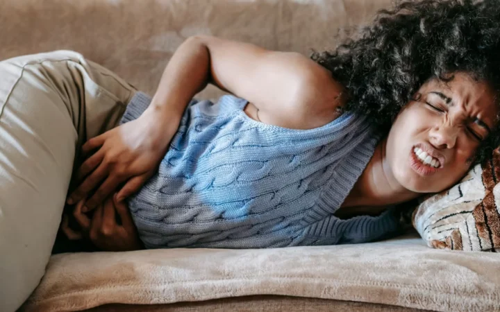 Young African American female lying on sofa in agony while having acute stomach ache