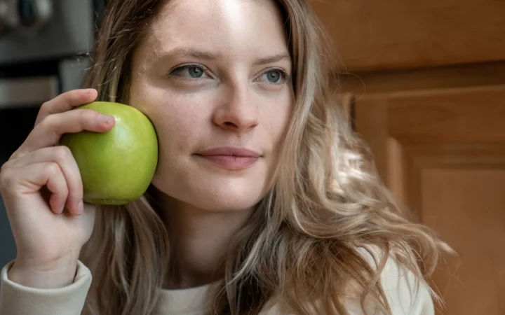 Close-up portrait of a woman indoors holding a green apple, showcasing natural beauty and health.