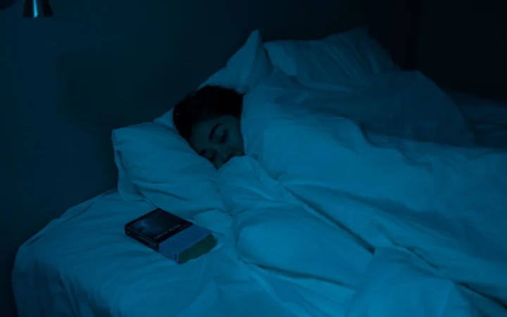 Woman peacefully sleeping with a book under blue night lighting, showcasing a cozy bedtime atmosphere.