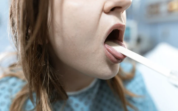 Close-up of a woman having her throat examined in a medical setting with a tongue depressor.