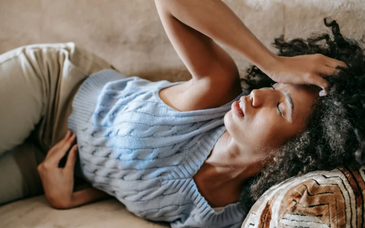 Young African American female lying on couch and touching forehead while having headache