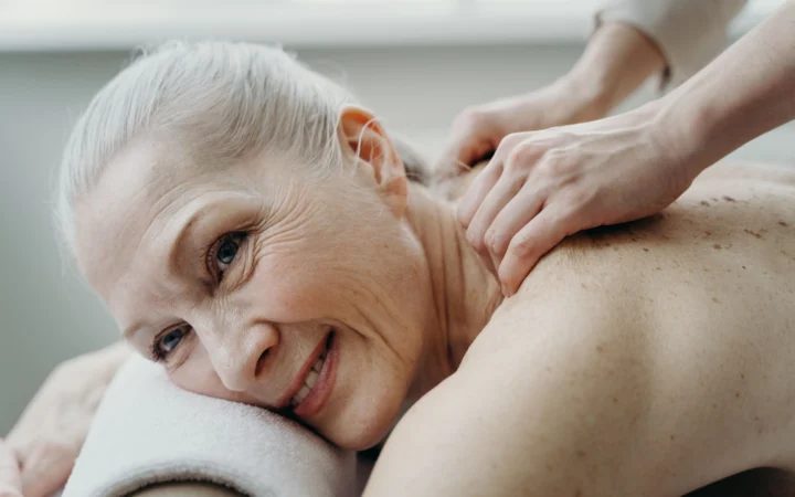 Senior woman with white hair smiles while receiving a therapeutic back massage indoors.