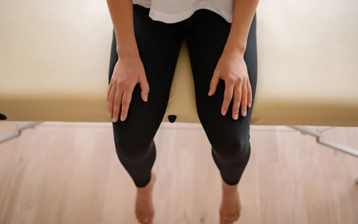 Woman sitting barefoot on a massage table indoors, captured from above.