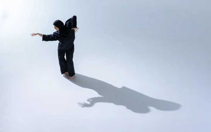 Female dancer in a hijab performs gracefully indoors, casting an artistic shadow.