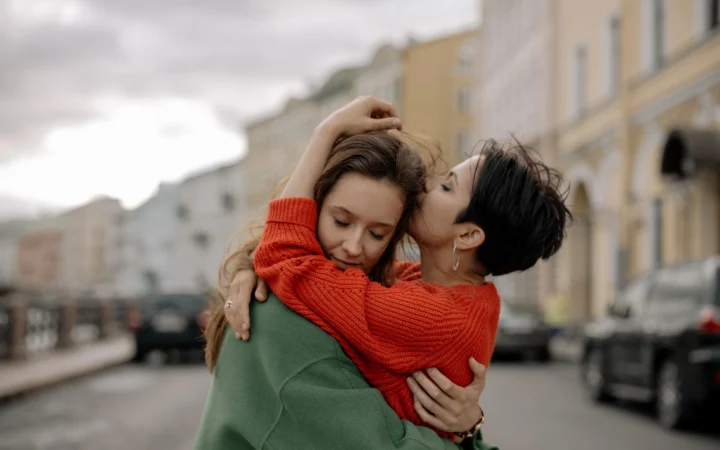Warm embrace between two women in a city setting, showcasing love and affection.