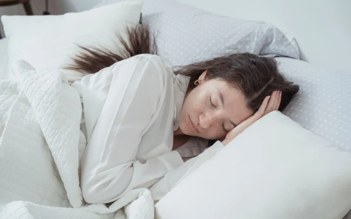 Serene woman rests comfortably in bed with soft pillows and blankets, embracing relaxation.