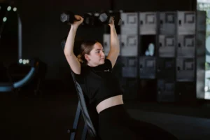 Young woman lifting dumbbells at gym showcasing strength training and fitness lifestyle.