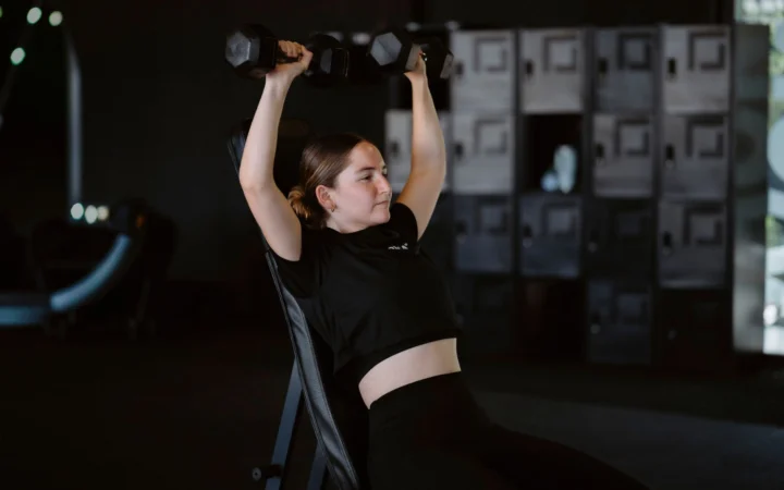Young woman lifting dumbbells at gym showcasing strength training and fitness lifestyle.